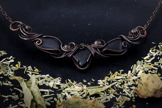 Antique copper necklace on a dark background with dried plants