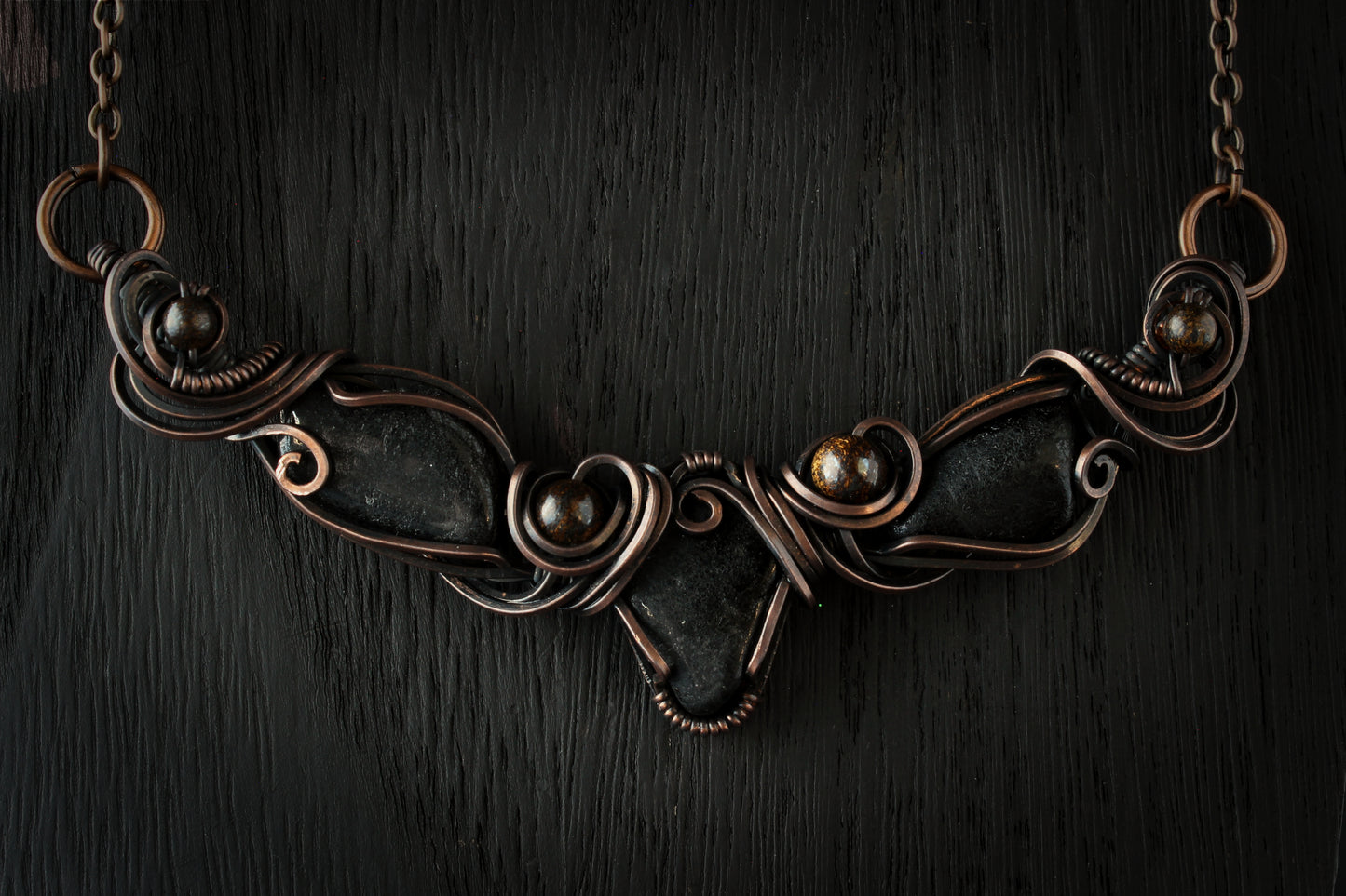 Oxidized copper necklace with dark stones on a dark wooden background