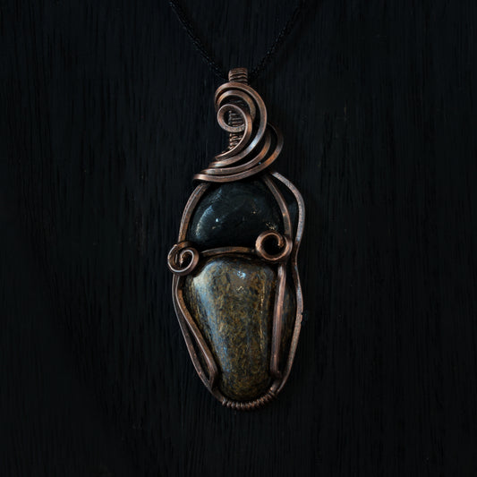 Pendant with black tourmaline & bronzite stones and oxidized copper wire wrapping on a dark background