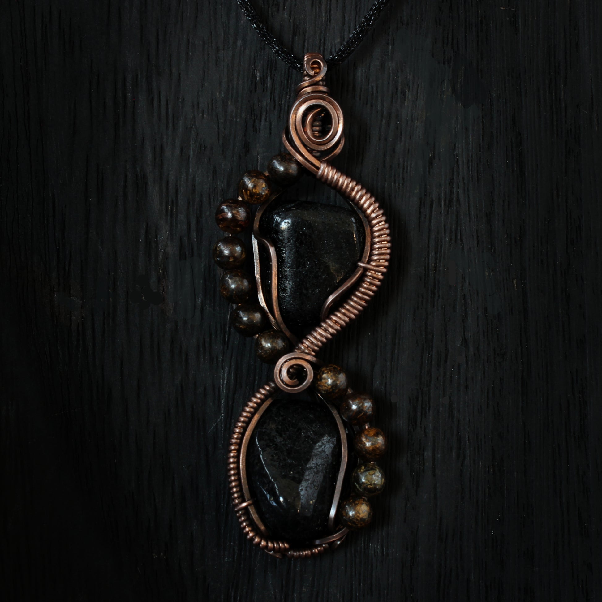 Pendant featuring black stones and copper wirework on a dark background