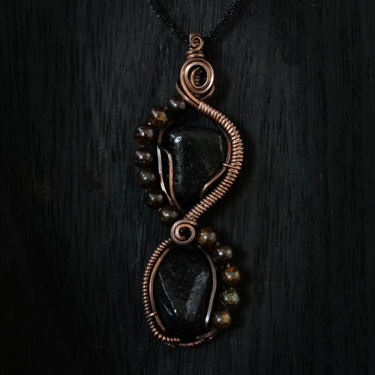 Pendant featuring black stones and copper wirework on a dark background