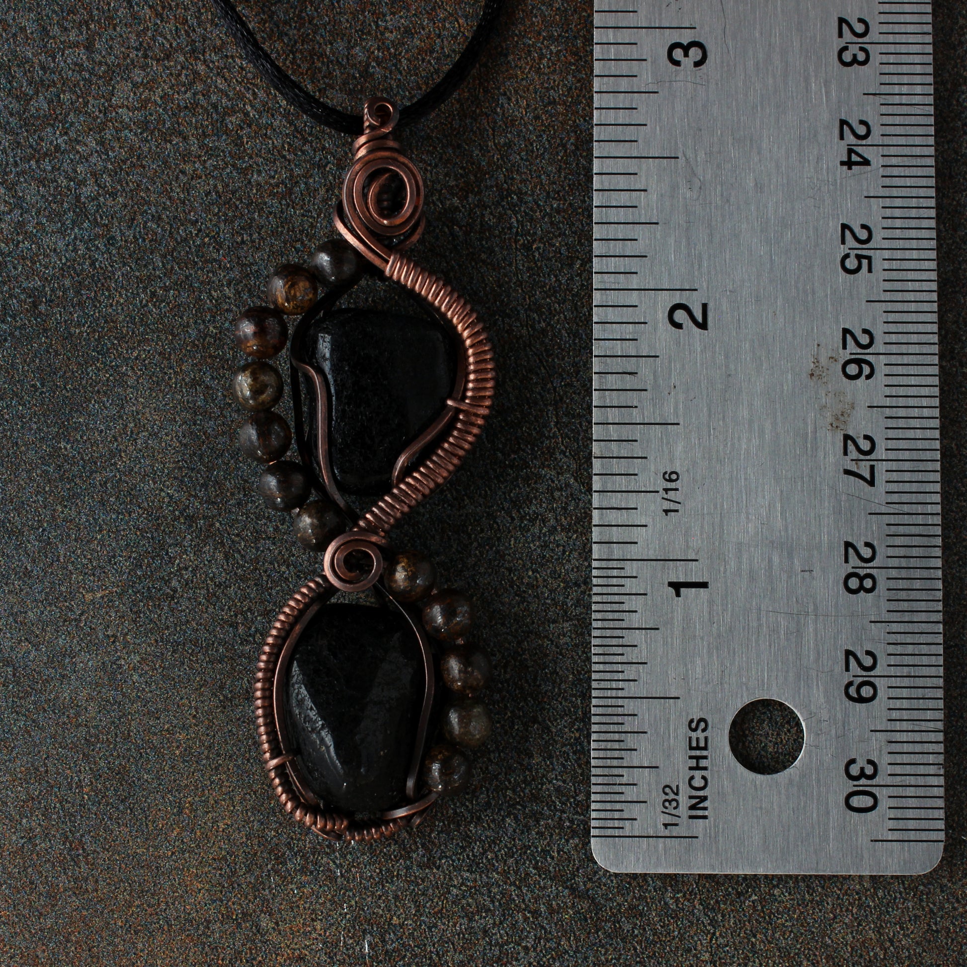 Copper and black stone pendant with a ruler for scale on a dark background