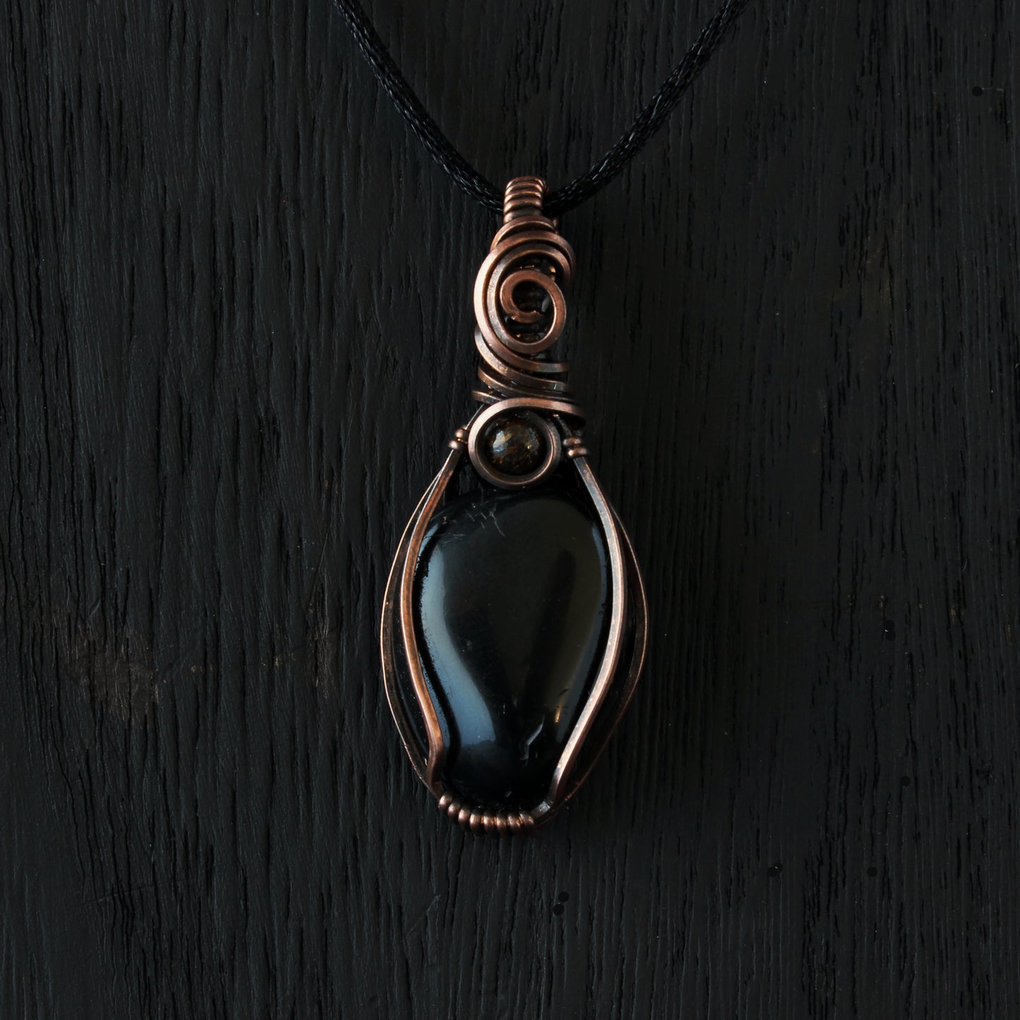 Black pendant with copper wire wrapping on a black background