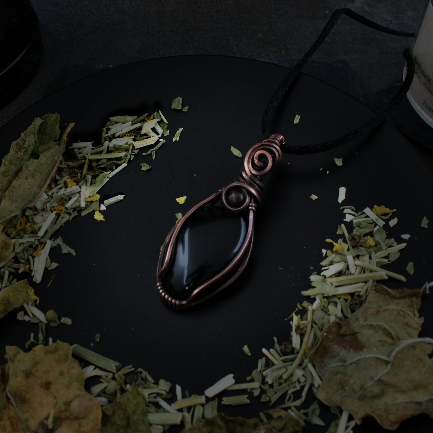 Copper pendant on a dark surface with dried herbs