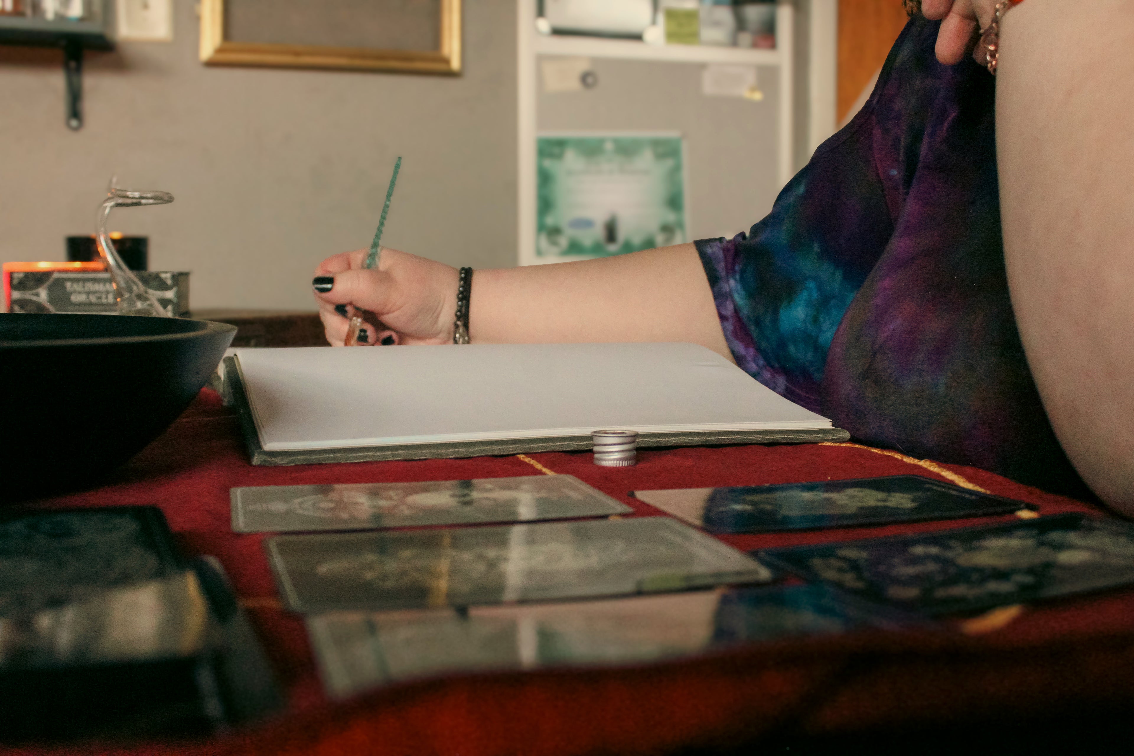 Person sitting at a table with oracle cards and a bowl, engaged in a reading.